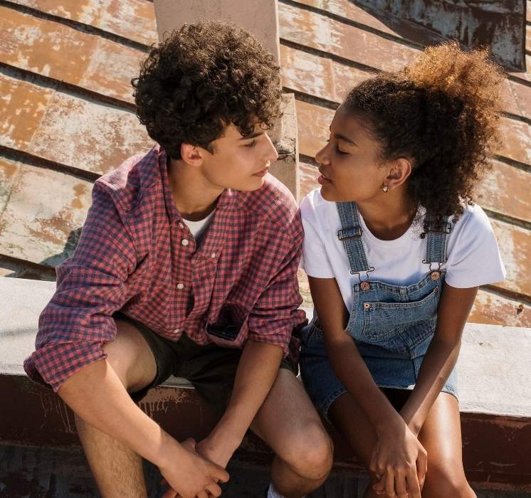 Deux adolescents, un garçon et une fille, assis côte à côte et discutant avec complicité pour l'atelier sur la puberté et la sexualité chez Pluri-elles, Winnipeg.