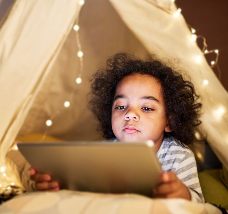 Enfant utilisant une tablette numérique sous une tente de jeu, illustrant la place des écrans et des appareils électroniques chez les jeunes avec Pluri-elles