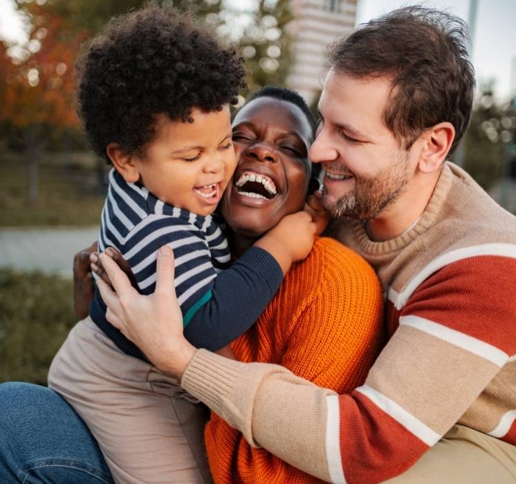 Famille heureuse et complice enlacée lors d'un atelier l'enfant au cœur de la famille pour l'épanouissement de l'enfant avec Pluri-elles
